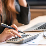 Person typing on calculator with pen in hand